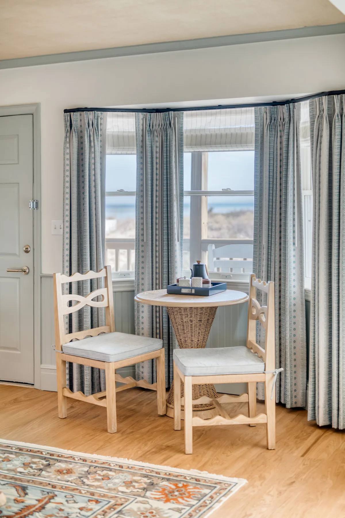 A cozy sitting area with a small round table, two wooden chairs, flowing curtains, and a decorative tray. The space is softly lit and perfect for intimate conversations or a quiet morning coffee, exuding warmth and relaxation.